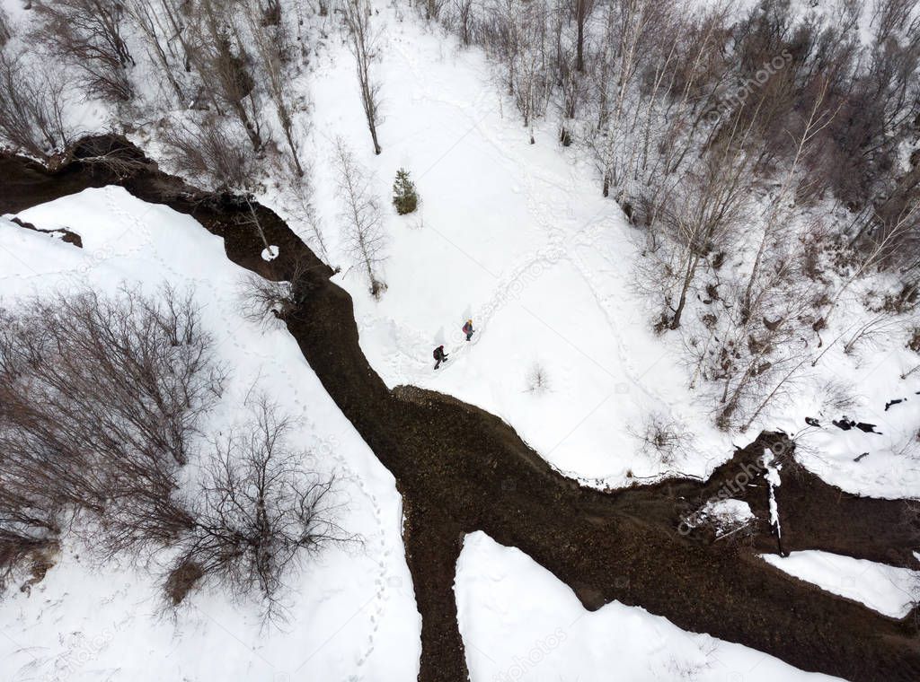 Couple of tourist is hiking in the mountain valley with river and snow at winter time in Almaty, Kazakhstan. Aerial top view, drone shot.