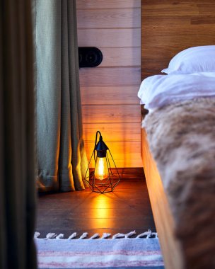 Oteldeki rahat yatak odasının modern iç mekanı. Ahşap zemininde parlayan tavan arası lambası var. 