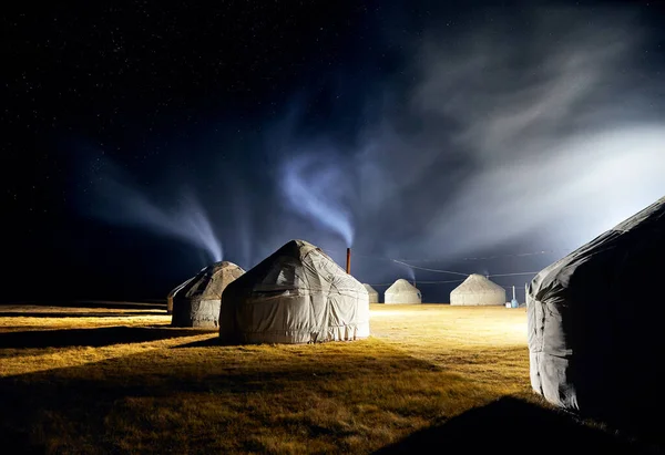 Yurt nomadic houses camp with smoke from the chimney at night sky with stars in Central Asia
