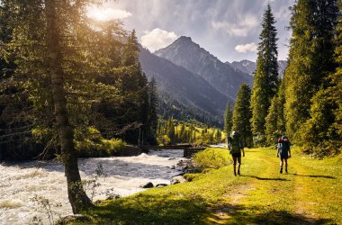 Two men with big backpacks is walking down the road in the forest of mountain valley in Karakol national park, Kyrgyzstan clipart