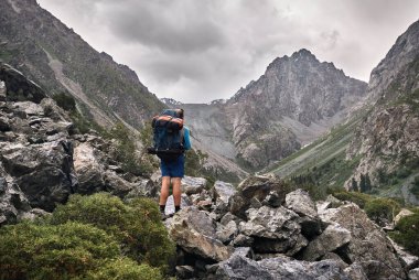 Büyük sırt çantalı turist, Kırgızistan 'daki Karakol Ulusal Parkı' ndaki dağ vadisinde kayalık yolda.