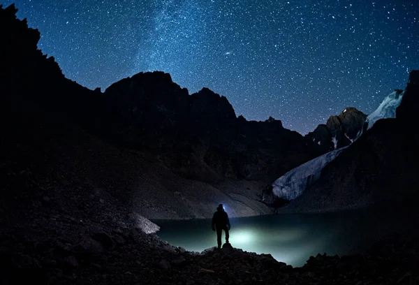 人头有光 在星夜的山中望着湖面 — 图库照片