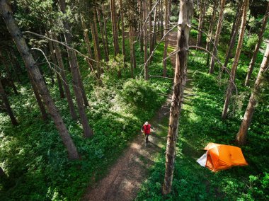 Dağlardaki ormanlarda turuncu çadırın yanında yürüyen bir adamın hava görüntüsü. Fotoğraf Drone ile çekildi