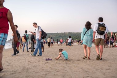 Arambol Beach, Goa, Hindistan - 24 Aralık 2016: sahilde turistler bir kalabalık içinde küçük bir çocuk oturur.