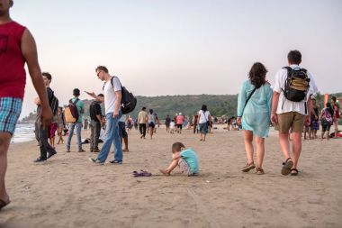 Arambol Beach, Goa, Hindistan - 24 Aralık 2016: sahilde turistler bir kalabalık içinde küçük bir çocuk oturur.