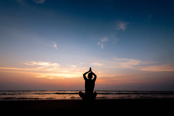 Young healthy man practicing yoga on the beach at sunset