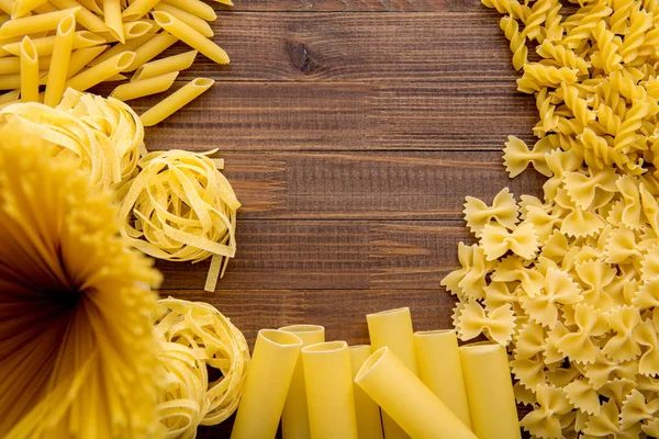 Různé druhy těstovin na dřevěném pozadí. Farfalle, fettuccin, nudle, fusilli a penne rigate. — Stock fotografie