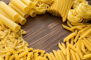 Ahşap arka planda farklı türde makarna. Farfalle, fettuccine, noodle, fusilli ve penne rigate..