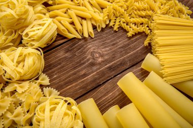 Ahşap arka planda farklı türde makarna. Farfalle, fettuccine, noodle, fusilli ve penne rigate..