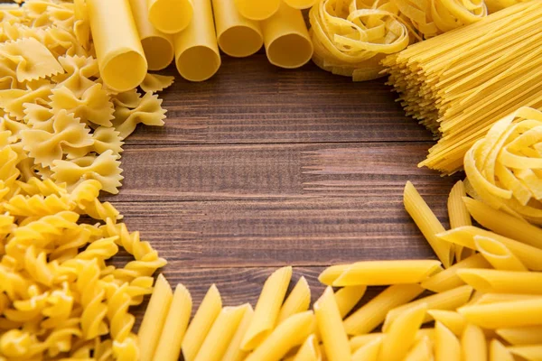 Diferentes tipos de macarrão em um fundo de madeira. Farfalle, fettuccine, macarrão, fusilli e penne rigate. Cozinha italiana saborosa . — Fotografia de Stock