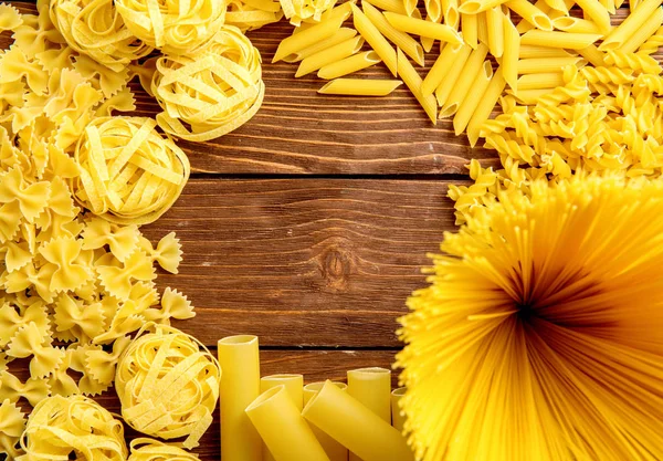 Diferentes tipos de macarrão em um fundo de madeira. Farfalle, fettuccine, macarrão, fusilli e penne rigate. Cozinha italiana saborosa . — Fotografia de Stock