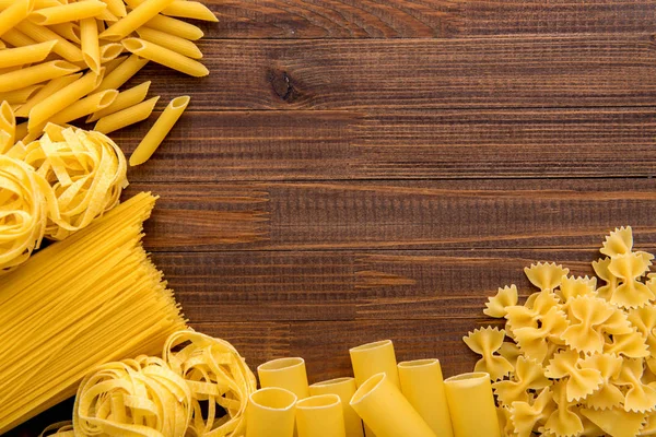 Ahşap arka plan üzerinde makarna çeşitleri. Farfalle, fettuccine, erişte, düdük ve penne rigate. Lezzetli İtalyan yemekleri.