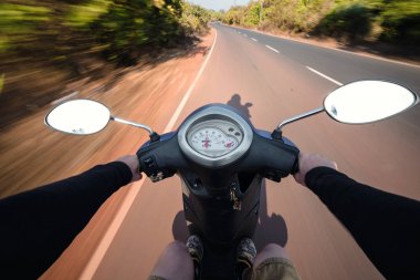 Scooter sürüş bir asfalt yolda binici. Hareketli arka plan bulanık. Birinci şahıs bakış.