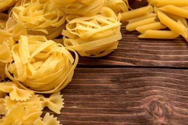 Ahşap arka plan üzerinde makarna çeşitleri. Farfalle, fettuccine, erişte, düdük ve penne rigate. Lezzetli İtalyan yemekleri