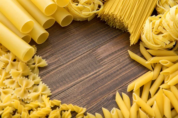 Diferentes tipos de macarrão em um fundo de madeira. Farfalle, fettuccine, macarrão, fusilli e penne rigate. Cozinha italiana saborosa — Fotografia de Stock