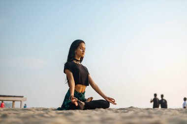 Genç sağlıklı kadın gün batımında plajda yoga yapıyor.