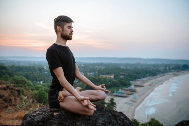 Sağlıklı adam gün batımında Yoga plaj altında uygulamak.