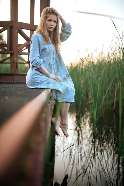 Romantisches Mädchen im blauen Kleid, das auf der Seebrücke sitzt. vegetativer Hintergrund — Stockfoto