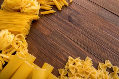 Ahşap arka planda farklı türde makarna. Farfalle, fettuccine, noodle, fusilli ve penne rigate..