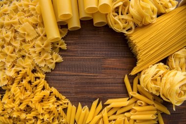 Ahşap arka planda farklı türde makarna. Farfalle, fettuccine, noodle, fusilli ve penne rigate..
