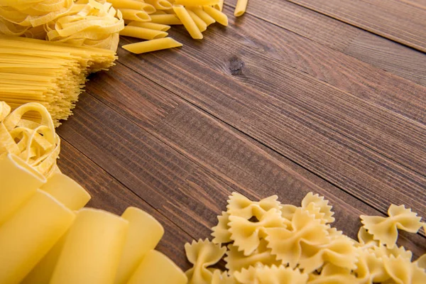 Diferentes tipos de macarrão em um fundo de madeira. Farfalle, fettuccine, macarrão, fusilli e penne rigate. — Fotografia de Stock