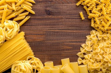 Ahşap arka planda farklı türde makarna. Farfalle, fettuccine, noodle, fusilli ve penne rigate..
