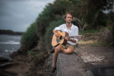 Sahilde gitar çalan romantik bir genç adam.