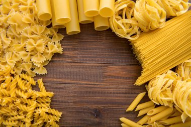 Ahşap arka planda farklı türde makarna. Farfalle, fettuccine, noodle, fusilli ve penne rigate..