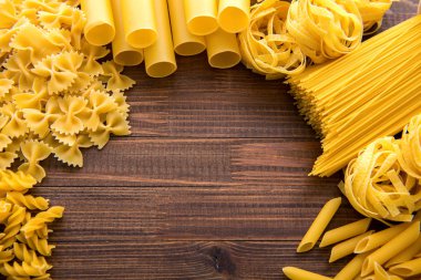 Ahşap arka planda farklı türde makarna. Farfalle, fettuccine, noodle, fusilli ve penne rigate..