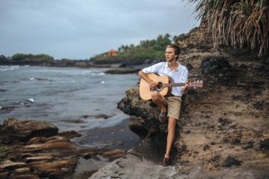 Sahilde gitar çalan romantik bir genç adam.