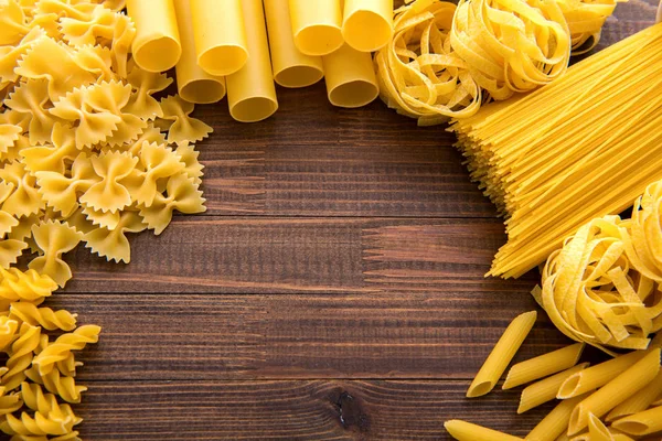 Diferentes tipos de macarrão em um fundo de madeira. Farfalle, fettuccine, macarrão, fusilli e penne rigate. — Fotografia de Stock