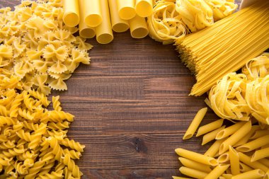 Ahşap arka planda farklı türde makarna. Farfalle, fettuccine, noodle, fusilli ve penne rigate..