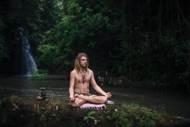 Yoga uygulaması ve doğada meditasyon. Nehir yakınlarında pratik yapan adam