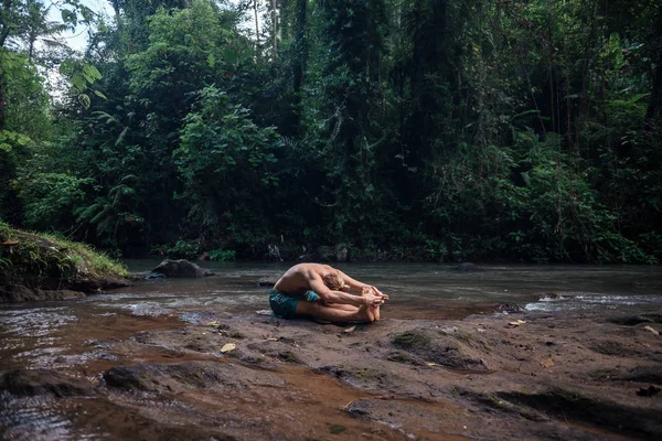 Yoga uygulaması ve doğada meditasyon. Nehir yakınlarında pratik yapan adam