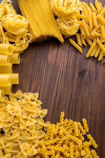 Olika typer av pasta på en trä bakgrund. Falle, fettuccin, nudlar, fusilli och penne vattna. — Stockfoto