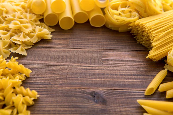 Different kinds of pasta on a wooden background. Farfalle, fettuccine, noodles, fusilli and penne rigate. — Stock Photo, Image