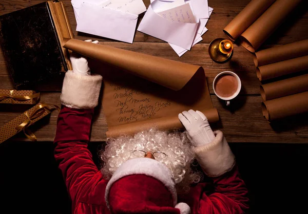Weihnachtsmann sitzt am Tisch in seinem Zimmer und liest Weihnachtsbrief oder Wunschzettel — Stockfoto