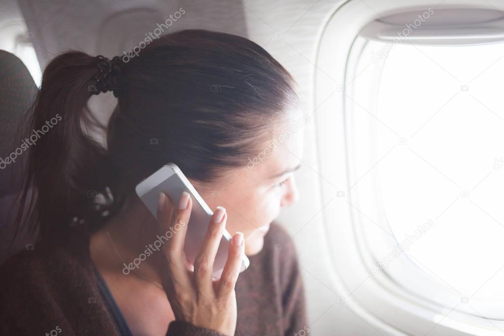 Woman on the airplane with smartphone looking in the porthole