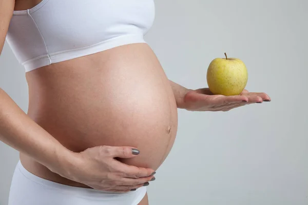 Barriga de uma mulher grávida com maçã verde na mão — Fotografia de Stock