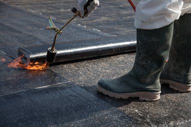 Düz beton yüzeydeki çatı malzemelerini kaplayan bir işçi.