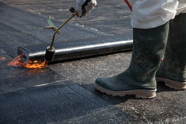 Düz beton yüzeydeki çatı malzemelerini kaplayan bir işçi. — Stok fotoğraf