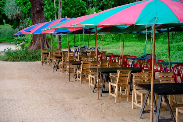 Café de plage avec tables et chaises en bois sous des parasols colorés — Photo