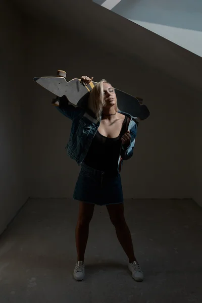 Vacker blond kvinna med longboard i mörkt rum — Stockfoto