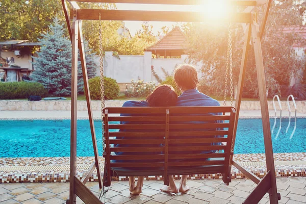 Belo jovem casal sentado no banco junto à piscina — Fotografia de Stock