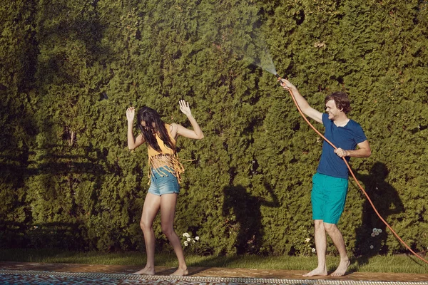 Couple having fun pour each other with garden hose — Stock Photo, Image