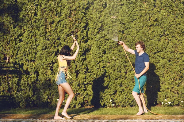 Couple having fun pour each other with garden hose — Stock Photo, Image