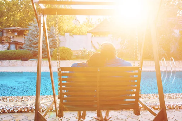 Belo jovem casal sentado no banco junto à piscina — Fotografia de Stock