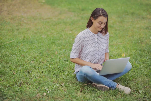 Молодая женщина с ноутбуком сидит на зеленой траве — стоковое фото