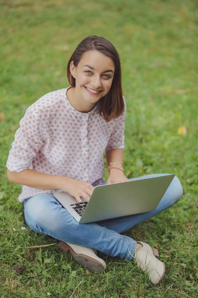 Young woman with laptop sitting on green grass — Stock Photo, Image