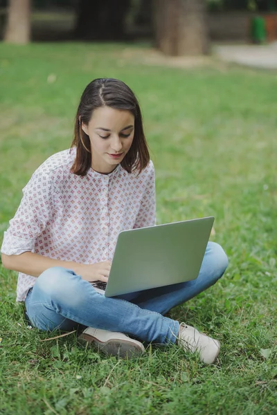 Junge Frau mit Laptop sitzt auf grünem Gras — Stockfoto